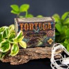 Mydlo-do-brody-Tortuga-110-g-w-opakowaniu-z-kolorowa-grafika.-Widoczny-napis-TORTUGA-z-fantazyjna-czcionka,-informacja-HANDCRAFTED-BEARD-SOAP.-Produkt-lezy-na-kawalku-drewna,-otoczony-zielonymi-liscmi,-na-ciemnym-tle..jpg