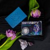 Mydlo-do-brody-w-blekitnym-kolorze-z-logo-RareCraft-na-ciemnym-tle.-W-tle-fioletowy-tulipan-i-ametyst.-Produkt-lezacy,-z-widoczna-etykieta-HANDCRAFTED-BEARD-SOAP-i-kolorowa-ilustracja-postaci..jpg