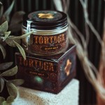 Balsam-do-brody-Tortuga-50-ml-w-przezroczystym-sloiku-z-czarna-nakretka-i-brazowo-zlota-etykieta.-Lezy-na-bialym-tle-obok-czarnego-opakowania-z-vintage-detalami.-W-tle-liscie-roslin..jpg