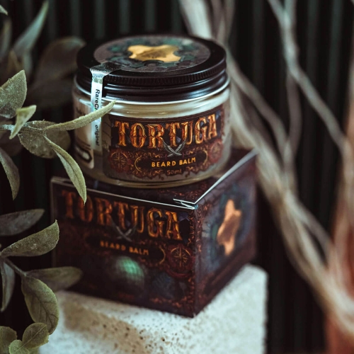 Balsam-do-brody-Tortuga-50-ml-w-przezroczystym-sloiku-z-czarna-nakretka-i-brazowo-zlota-etykieta.-Lezy-na-bialym-tle-obok-czarnego-opakowania-z-vintage-detalami.-W-tle-liscie-roslin..jpg